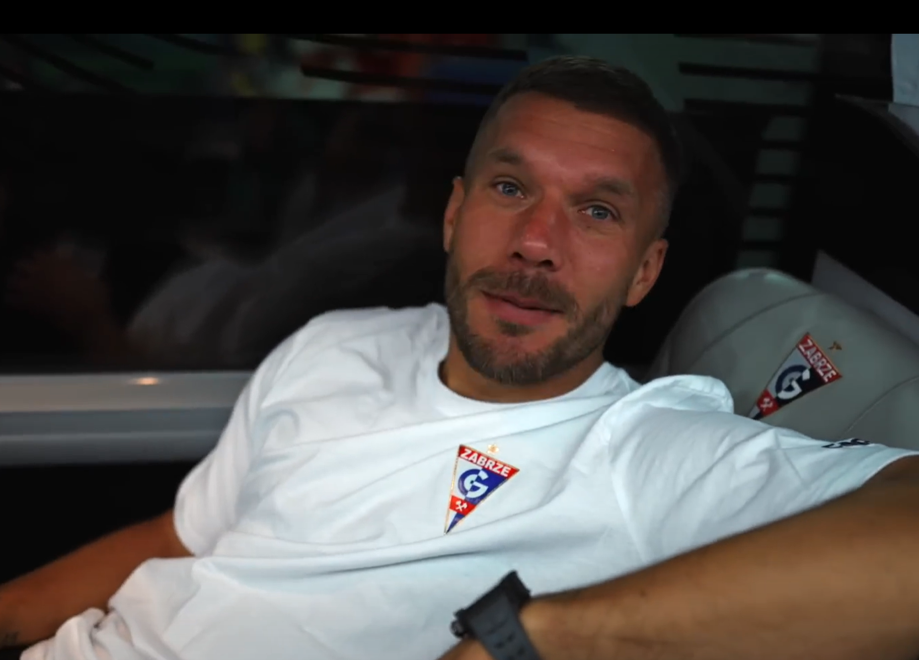 Lukas Podolski sitzt entspannt in einem Auto in einem Trikot von Gornik Zabrze.